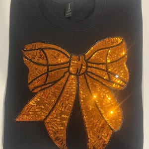 May include: Black sweatshirt with a large orange sequined bow on the front.
