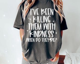Op de afbeelding: Donkergrijs t-shirt met de witte tekst: "I'VE BEEN KILLING THEM WITH KINDNESS WHEN DO THEY DIE?". Het shirt heeft een ronde hals en korte mouwen. Het shirt wordt gedragen met een grijze short.
