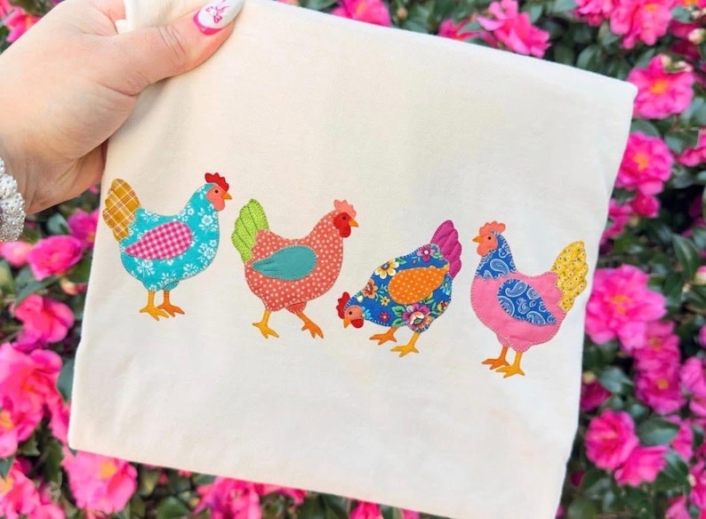 Op de afbeelding: Een cr&egrave;mekleurige draagtas met vier kleurrijke kippenapplicaties. Elke kip heeft een uniek patroon, waaronder bloemen- en stippenontwerpen. De kleuren zijn blauw, roze, oranje en rood, met gele poten en rode kammen.