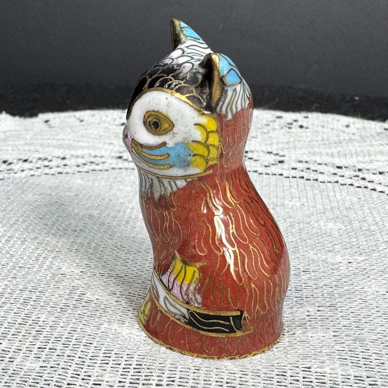 May include: A small, decorative owl figurine with a red body and a white face. The owl's head features black, blue, and yellow accents. Gold-colored details outline the design. The figurine is made of a glossy material.