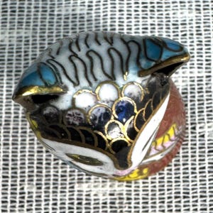 May include: A detailed, hand-painted miniature fish figurine. The fish features a blue, white, and black body with gold accents. The figurine is likely made of enamel or a similar material, showcasing intricate patterns and colors.