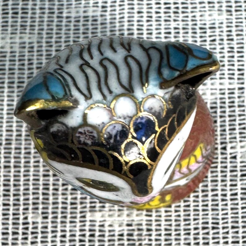 May include: A detailed, hand-painted miniature fish figurine. The fish features a blue, white, and black body with gold accents. The figurine is likely made of enamel or a similar material, showcasing intricate patterns and colors.