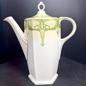 May include: A white porcelain coffee pot with a hexagonal body and a matching lid featuring a ring-shaped handle. The upper section is decorated with a green and pale yellow floral pattern, accented by thin gold trim along the edges and spout.