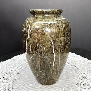 May include: A decorative vase with a dark green and brown marble pattern, featuring white veining throughout. The vase has a rounded body and a slightly flared rim. The surface is glossy, reflecting light.