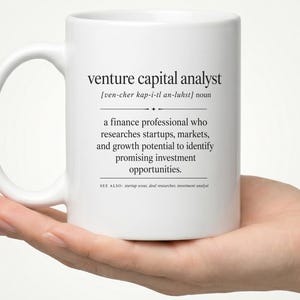 Puede incluir: Una taza de cerámica blanca con texto impreso en negro que define a un analista de capital riesgo como un profesional de las finanzas que investiga startups, mercados y potencial de crecimiento para identificar oportunidades de inversión.