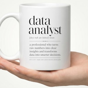 May include: A white ceramic mug featuring black printed text that defines a data analyst as a professional who turns raw numbers into clear insights and transforms data into smarter decisions, including phonetic pronunciation and related terms.