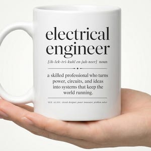 May include: A white ceramic mug featuring black printed text that defines an electrical engineer as a skilled professional who turns power, circuits, and ideas into systems that keep the world running, including phonetic spelling and related terms.