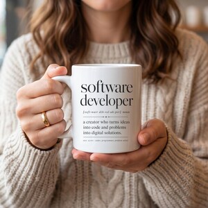 White mug with "Software developer" definition, held by a person.