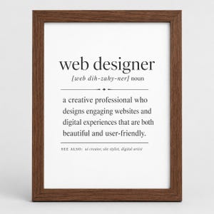 Peut inclure: Une affiche encadrée présentant une définition de type dictionnaire du terme web designer. Le texte est imprimé en noir sur un fond blanc, dans un cadre en bois brun foncé. La définition décrit un professionnel de la création.