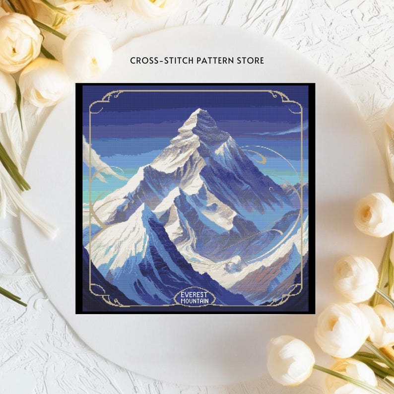 May include: Cross-stitch pattern of Mount Everest, a snowy mountain peak with a blue sky and clouds. The pattern is framed in a gold border and includes the text "EVEREST MOUNTAIN".