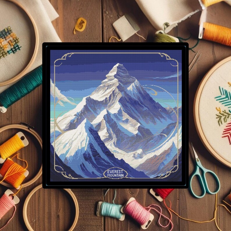 May include: A framed cross-stitch pattern of Mount Everest, a snow-capped mountain range with a blue sky background. The text "EVEREST MOUNTAIN" is at the bottom of the image.