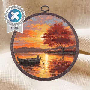 K&ouml;nnte beinhalten: Eine Kreuzstich-Stickerei, die eine Sonnenuntergangsszene mit einem einsamen Boot auf einem See zeigt. Der Himmel ist in leuchtenden Orange- und Gelbt&ouml;nen gehalten, im Vordergrund steht ein einzelner Baum. Das Boot befindet sich in der Mitte des Sees, mit einer Person, die es rudert.