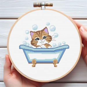 May include: A brown and white cat with blue eyes is having a bath in a blue bathtub. The cat is surrounded by white bubbles.