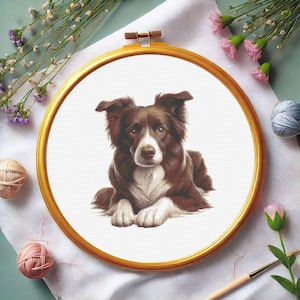 Könnte beinhalten: Kreuzstich-Stickerei eines braun-weißen Border Collie-Hundes in einem goldenen Stickrahmen. Der Hund liegt mit gekreuzten Pfoten. Der Hintergrund ist weiß. Blumen und Nähutensilien umgeben den Rahmen.