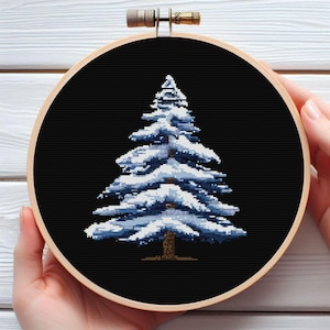 May include: A snowy blue pine tree cross-stitch pattern on black fabric in a wooden embroidery hoop.