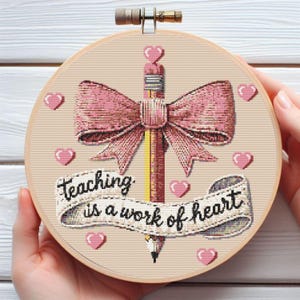 May include: A round embroidery hoop with a pink and white bow, a pencil, and the text "Teaching is a work of heart".