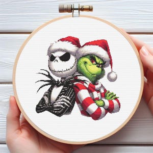 Può includere: Ricamo a punto croce in un telaio di legno con Jack Skellington e il Grinch con cappelli di Babbo Natale. Jack è in bianco e nero, e il Grinch è verde, entrambi con le braccia incrociate. Lo sfondo è bianco.