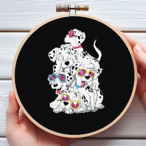 Peut inclure: Un cercle de broderie au point de croix avec un motif de chiens dalmatiens. Les chiens sont blancs avec des taches noires et portent des lunettes de soleil. Le fond est noir et le cercle est en bois.