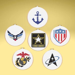 May include: A collection of seven cross-stitch embroidery hoops featuring military and service branch emblems. Designs include an anchor, an eagle, a star, and a shield, all in patriotic colors. Each design is set against a white background.
