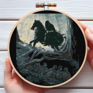 Może przedstawiać: Haft krzyżykowy w drewnianym tamborku przedstawia mroczną scenę z jeźdźcem na koniu w lesie. Dzieło przedstawia czarnego konia i jeźdźca, ze szczegółowym tłem drzew i postaci. Tamborek jest trzymany przez ręce.