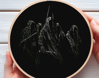 May include: A black cross-stitch embroidery hoop depicting cloaked figures with weapons. The artwork is set against a black background, framed by a wooden hoop. The piece is held by a person's hands.