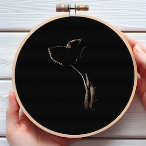 May include: A cross-stitch embroidery hoop featuring a profile of a dog against a black background. The dog is rendered in shades of brown, with the hoop made of light-colored wood. The design is centered within the round frame.