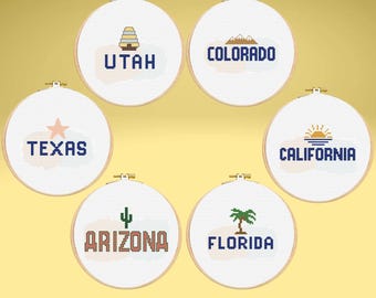 May include: A collection of six cross-stitch hoops, each featuring a state name and a related icon. States include Utah, Colorado, Texas, California, Arizona, and Florida. The text and icons are in shades of blue, brown, and green, set against a white background.