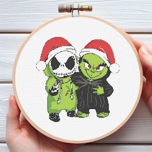 May include: A cross-stitch embroidery hoop featuring two cartoon characters wearing Santa hats. One is a green Grinch-like figure, and the other is Jack Skellington from The Nightmare Before Christmas. The characters are in green and black, with red and white Santa hats.
