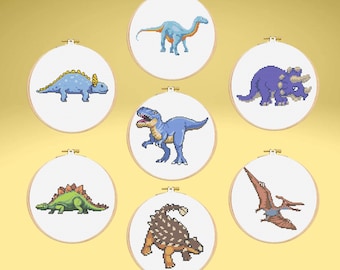 Pode incluir: Uma coleção de sete bastidores de bordado em ponto cruz de dinossauros. Cada bastidor apresenta um dinossauro diferente em um estilo pixelizado, incluindo um Brontossauro azul, um Triceratops roxo e um Estegossauro verde. Os bastidores estão em um fundo dourado.