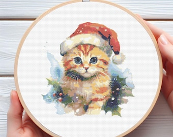 May include: Cross-stitch embroidery of a ginger kitten wearing a Santa hat, surrounded by holly and berries. The artwork is displayed in a wooden embroidery hoop, perfect for holiday decor or a cat lover's gift.