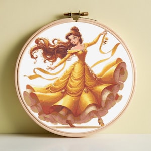 May include: A cross-stitch embroidery of a woman in a yellow gown, dancing. The woman has long brown hair and is holding a ribbon. The embroidery is set in a wooden hoop.