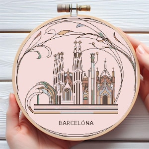 May include: A pink and white cross-stitch embroidery hoop with a detailed illustration of the Sagrada Familia in Barcelona, Spain. The text "BARCELONA" is printed below the illustration.