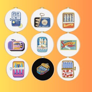 May include: Nine cross-stitch embroidery hoops featuring sardine can designs. Each hoop showcases a different illustration of sardines in various can styles, with vibrant colors and detailed stitching. The designs include text such as "Sardines" and "De Loctudy".