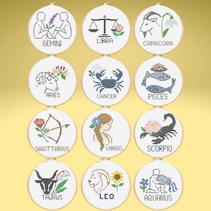 May include: A set of twelve cross-stitch embroidery hoops, each depicting a different zodiac sign. Signs include Gemini, Libra, Capricorn, Aries, Cancer, Pisces, Sagittarius, Virgo, Scorpio, Taurus, Leo, and Aquarius, with their symbols and names.