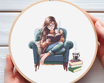 May include: A woman wearing glasses sits in a blue armchair reading a book and holding a cup of coffee. She is wearing a blue sweater and jeans. There are books stacked on a table next to her.