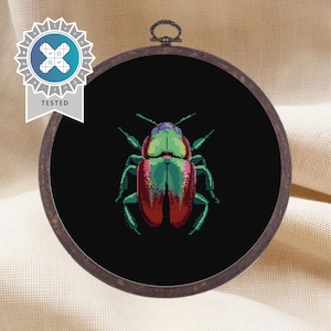 May include: A round embroidery hoop with a black background and a colorful beetle design. The beetle is green, red, and black with a metallic sheen.