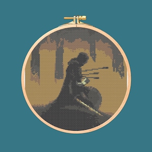 May include: A cross-stitch embroidery hoop featuring a pixelated image of a figure in a dark cloak, possibly a knight or warrior, with arrows. The background has a sepia tone with a teal background.