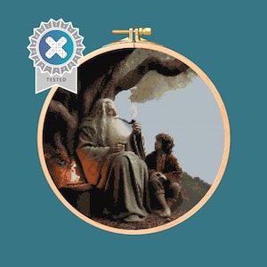 May include: A cross-stitch embroidery hoop featuring a scene from The Lord of the Rings. Gandalf is seated, smoking a pipe, with Frodo nearby. The artwork is framed in a wooden hoop, with a "TESTED" badge.