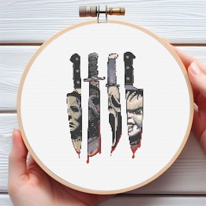 May include: A cross-stitch embroidery hoop featuring four knives with horror movie character faces. The knives are in black, gray, and white, with red blood details. The embroidery is set against a white background.