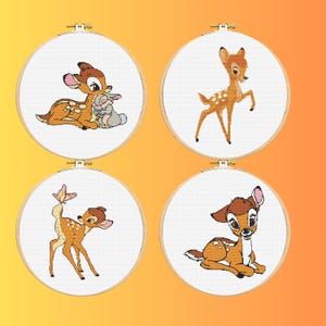 May include: Four cross-stitch embroidery hoops featuring Bambi and friends. Each hoop has a white background with a different image of Bambi, Thumper, and a butterfly. The hoops are set against an orange and yellow gradient.