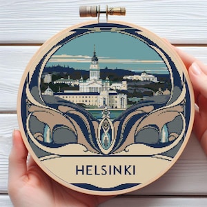 May include: A round embroidery hoop with a blue background and a white border. The centre of the hoop features a colourful image of the Helsinki skyline with the text "HELSINKI" below the image.