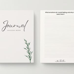 May include: A white journal with a black spiral binding and the text "Journal Shadow Work" on the cover. The cover also features a green leafy branch illustration. The opposite page has lined paper and the text "What emotions do I avoid feeling, and why do I resist them?"