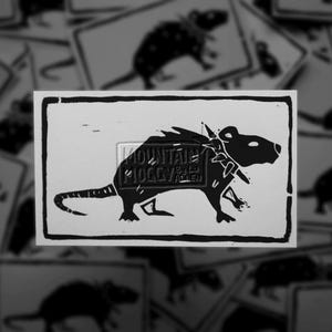 May include: A rectangular black and white print featuring a stylised rat wearing a spiked collar. The rat is depicted in profile facing right, enclosed within a thick black border. The text MOUNTAIN MOGGY BY LU ALLEN is visible in the centre.