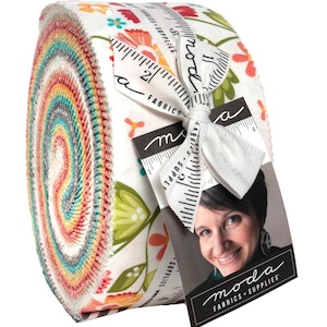 May include: A roll of colorful fabric strips, tightly wound and secured with a white ribbon and tag. The fabric features a floral pattern with red, orange, green, and blue hues. The tag includes the text "moda FABRICS + SUPPLIES".