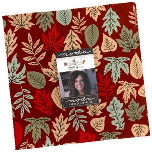 May include: A square fabric swatch featuring a deep red background with a repeating pattern of autumn leaves in shades of sage green, cream, and bright red. A Moda Windfall fabric label is centered on the fabric, showing a 5-inch ruler scale.