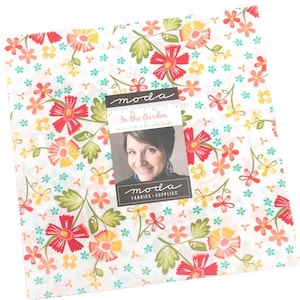 May include: A square fabric bundle with a floral pattern in red, yellow, and green on a white background. The fabric is decorated with small blue flowers. A label with the text "In the Garden" and a woman's portrait is attached.