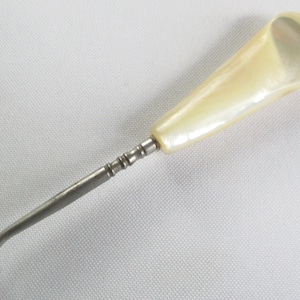 May include: A silver shoe horn with a white pearl handle. The handle is shaped like a teardrop.
