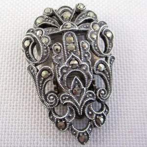 Puede incluir: Un broche plateado con un dise&ntilde;o floral detallado, engastado con piedras de marcasita.