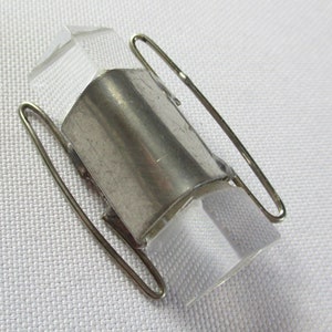 May include: A silver metal ring with two clear glass pieces on either side. The ring is held together by a wire loop.