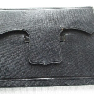 May include: A black rectangular case with a textured surface. It features a flap closure with a curved design and a small tab. The case is likely made from a durable material.